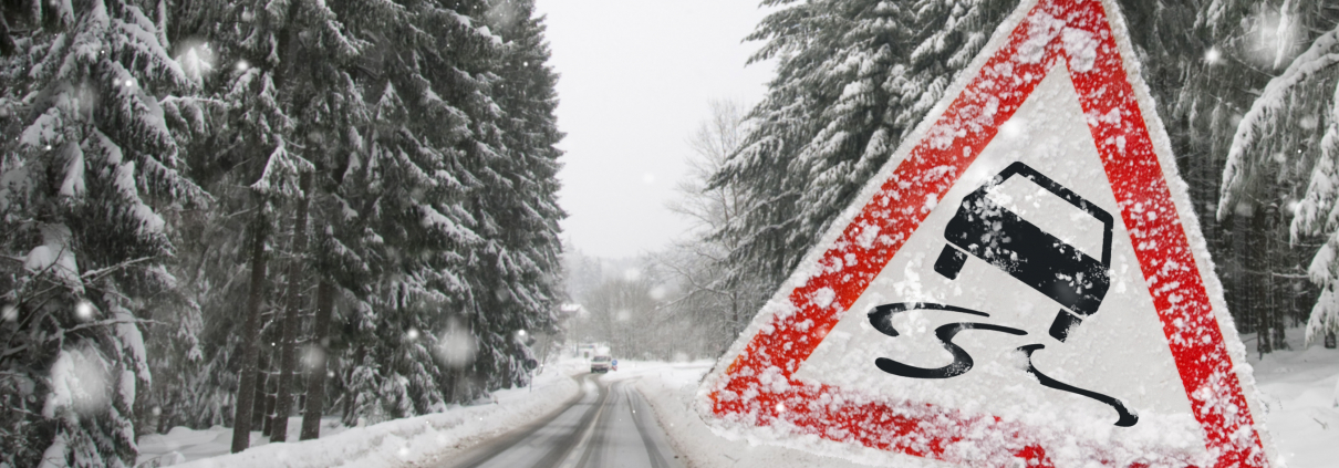 Auf einer verschneiten Straße befinden sich rechts und links verschneite Tannen und im Vordergrund ein Warnschild für Rutschgefahr
