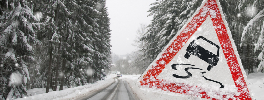 Auf einer verschneiten Straße befinden sich rechts und links verschneite Tannen und im Vordergrund ein Warnschild für Rutschgefahr